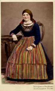 Kolorerat porträtt av sittande kvinna i folkdräkt.Skåne - Nordiska Museet - NMA.0039751