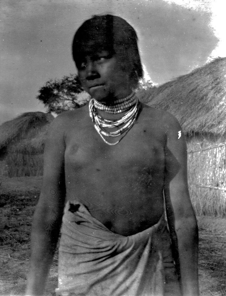 Korthårig flicka med halsband. I bakgrunden syns hyddor. Gran Chaco. Bolivia - SMVK - 004754