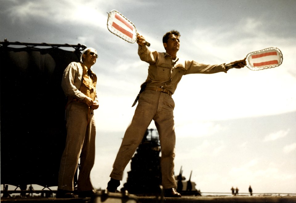 Landing Signal Officer aboard USS Lexington (CV-16), gives an incoming pilot the signal to lift one wing, circa November-December 1943 (80-G-K-15601)