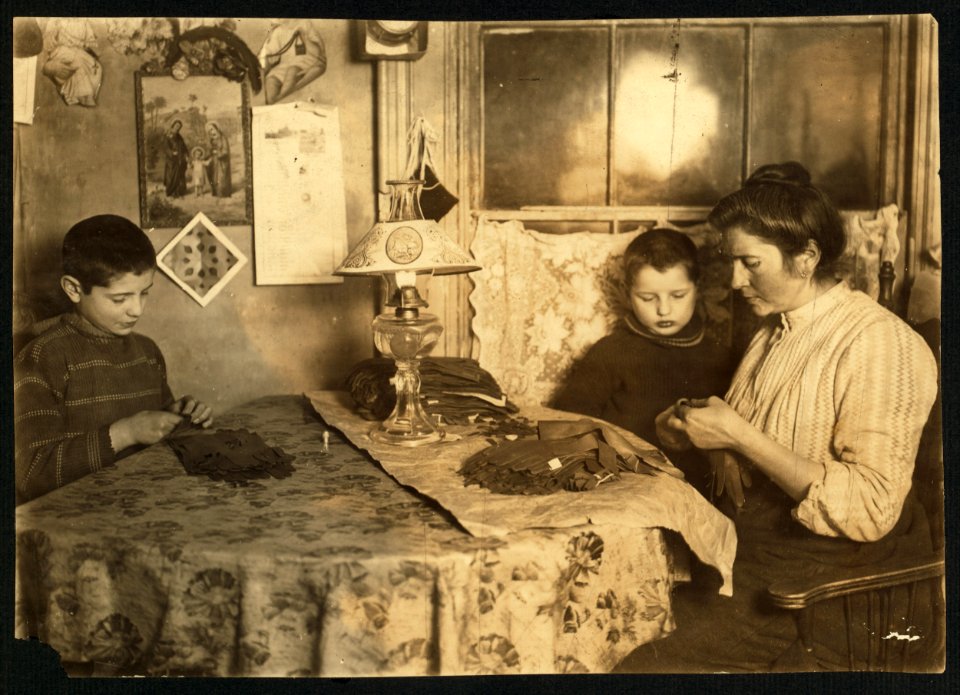 Late at night. Sewing tapes on gloves. The boy helps. Family of five sleep in room where the work is done. LOC cph.3a26906