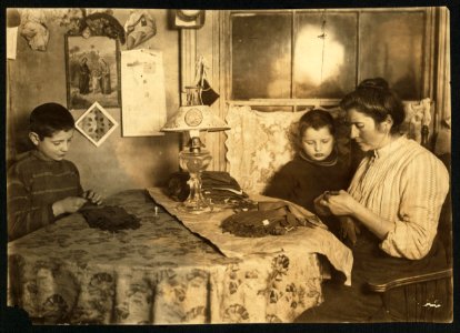 Late at night. Sewing tapes on gloves. The boy helps. Family of five sleep in room where the work is done. LOC cph.3a26906