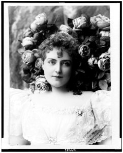 Lillian Russell, head-and-shoulders portrait, facing front in lace dress with bouquet of roses behind her head LCCN91796074