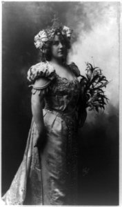 Lillian Russell, three-quarter length portrait, standing, facing right, holding flowers LCCN92521079