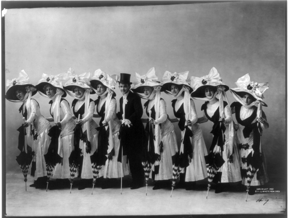 Line of 8 chorus girls with top-hatted man in middle LCCN2004678704