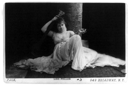 Loie Fuller, full length, seated, facing front; holding cigarette and stringed musical instrument LCCN2005683740