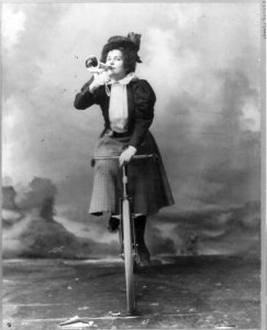 Madge Lessing, full length, on bicycle, facing left; holding musical horn to lips LCCN2005684803