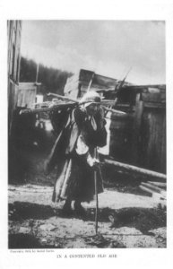 Makah woman carrying firewood near buildings, Neah Bay, Washington, ca 1910 (CURTIS 2119)