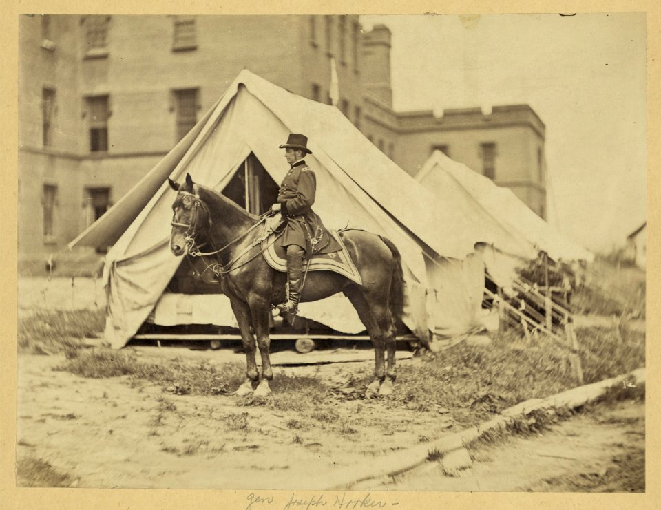 Major-General Joseph Hooker, full-length portrait, seated on horse, facing left, wearing military uniform, two tents and large building in the background LCCN2008680203