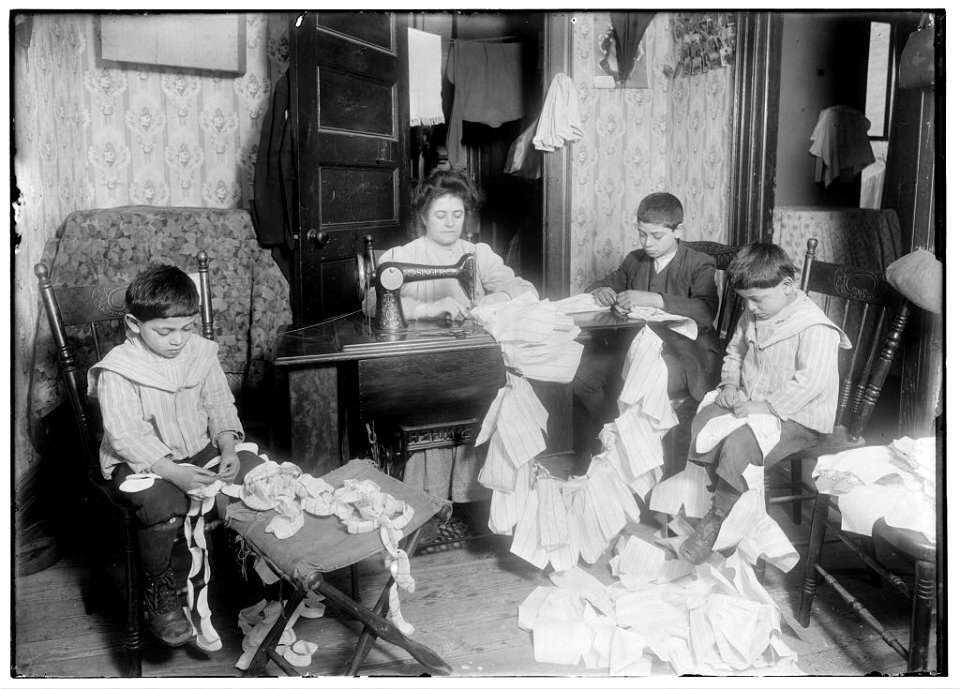 Making dresses for Campbell Kid Dolls in a dirty tenement room, 59 Thompson St., N.Y. 4th floor front. Romana family. The older boy, about 12 years old, operates the machine when the mother LOC nclc.05492