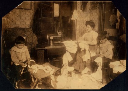 Making dresses for Campbell Kid Dolls in a dirty tenement room, 59 Thompson St., N.Y., 4th floor, front-Romana family. The little boys, 5 and 7 years old, help to break the threads, the LOC nclc.04216