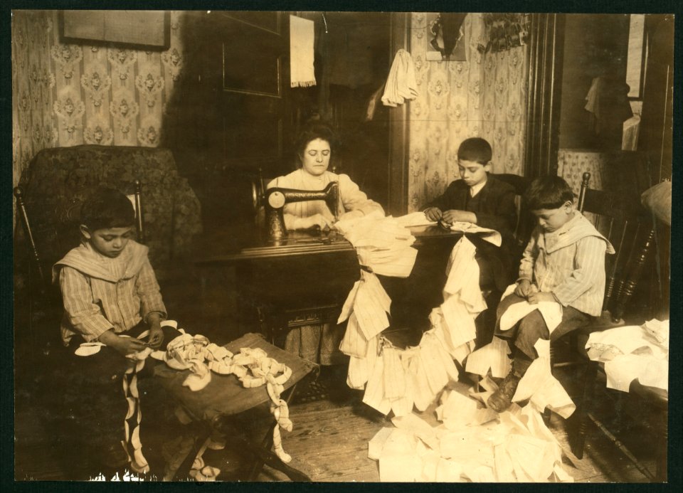 Making dresses for Campbell Kid Dolls in a dirty tenement room, 59 Thompson St., N.Y. 4th floor front. Romana family. The older boy, about 12 years old, operates the machine when the mother LOC nclc.05492