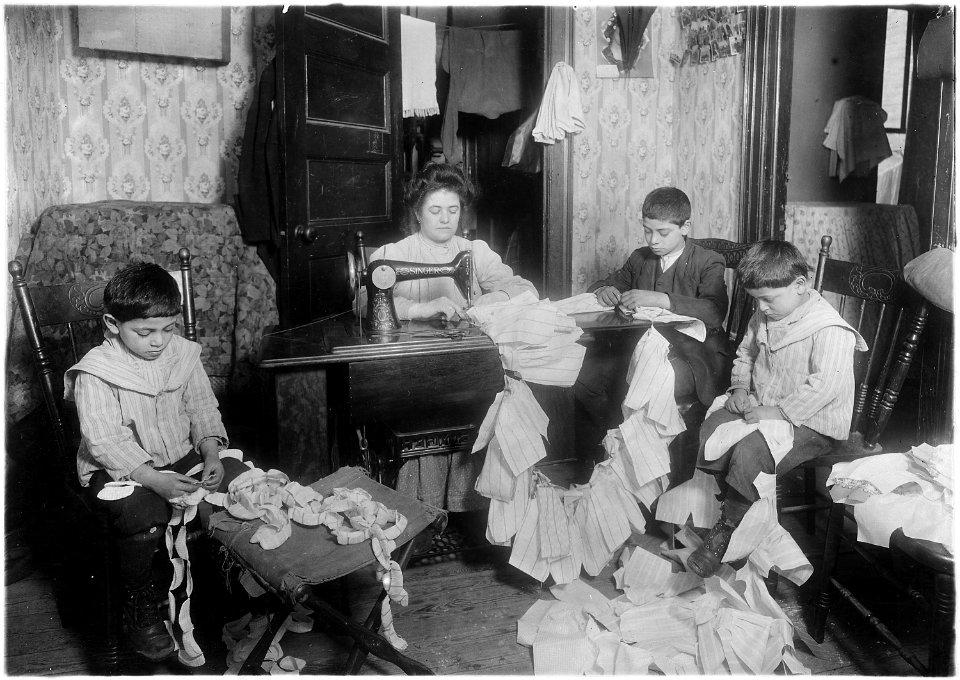Making dresses for Campbell kids dolls in a dirty tenement. The older boy, about 12 years old, operates the machine... - NARA - 523529