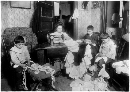 Making dresses for Campbell kids dolls in a dirty tenement. The older boy, about 12 years old, operates the machine... - NARA - 523529