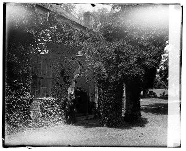 Man standing by the doorway of an old vine-covered building LCCN2016828299