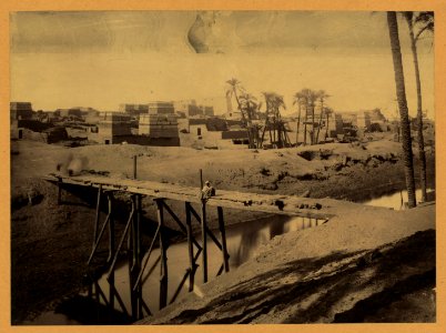 Man seated on wooden bridge over canal, ruins and buildings in background LCCN2004674247