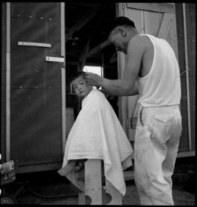 Manzanar Relocation Center, Manzanar, California. Little evacuee of Japanese ancestry gets a haircut. - NARA - 538083 photo