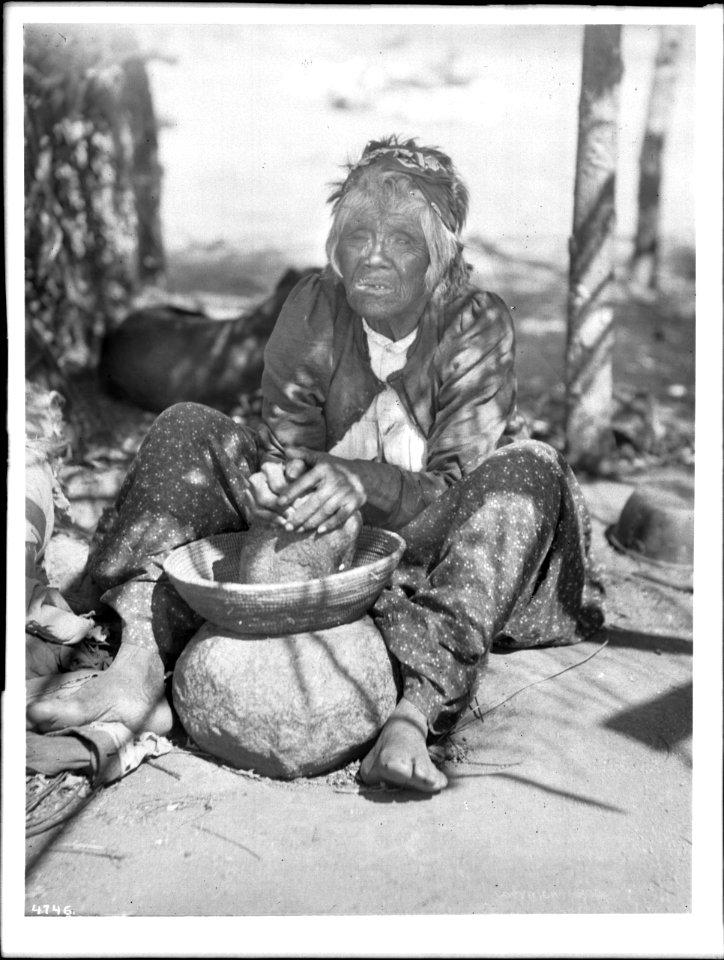 Maria Casseri, a Coahuilla Indian woman, grinding mesquite beans for flour on a stone metate with a basket top, California, ca.1899 (CHS-4746)