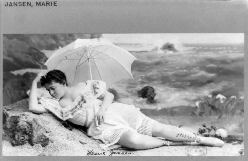 Marie Jansen, full-length portrait, in studio beach scene, facing left, smoking cigarette and holding umbrella LCCN89706397