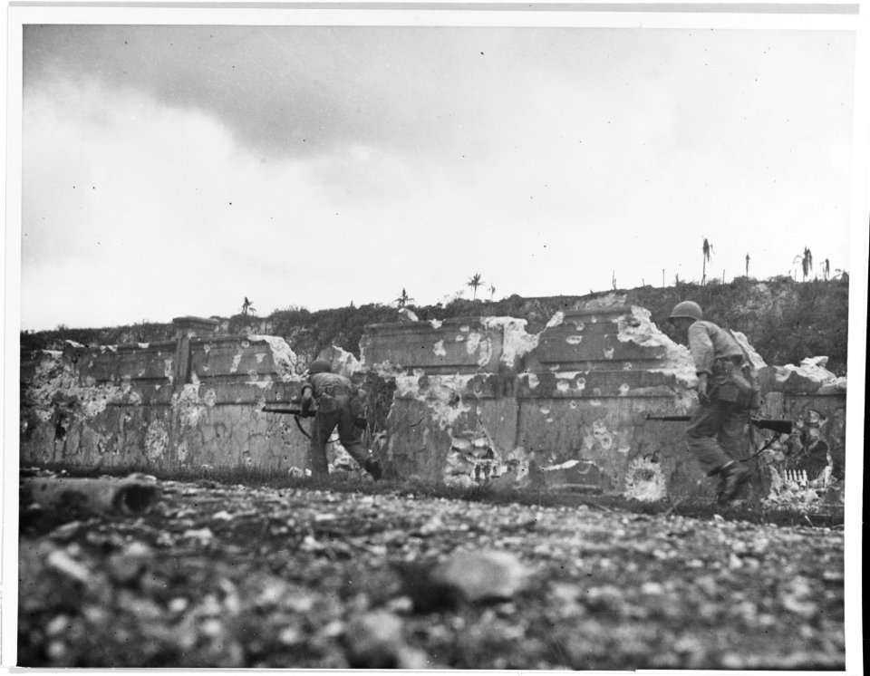 Marines under cover of a wall near a Guam cemetery, 1944