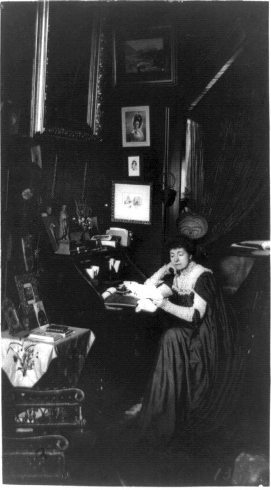 Mme. Helena Modjeska, full-length portrait, seated at desk, facing left, surrounded by pictures LCCN90707063