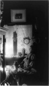 Mme. Helena Modjeska, half-length portrait, seated at small table by window, facing left, surrounded by vases, wreaths, and picture LCCN90707061