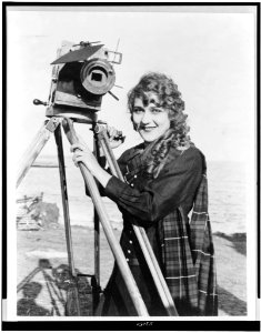 Mary Pickford, half-length portrait, standing, facing slightly left, with motion picture camera, on beach LCCN95502963