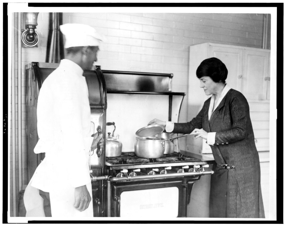 Mary Roberts Rinehart, lifting lid of pot on stove, and chef standing alongside LCCN93508074