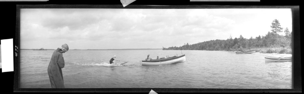 Motorboat towing wakeboard, robed figure on shore LCCN2017656414