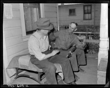 Mr. Irving Bittick, miner, tells a friend how long the big fish was that got away. He is shown on the front proch of... - NARA - 540523