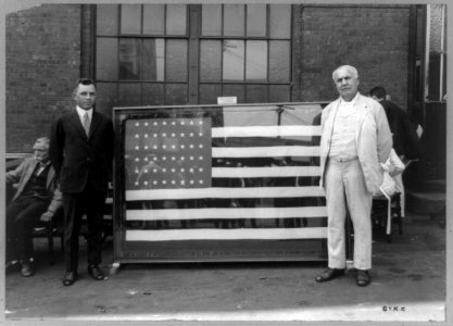 Mr. Thomas A. Edison standing next to flag presented to him for the forty-third anniversary of the Ediphone invention by Ediphone Distributors LCCN89714705