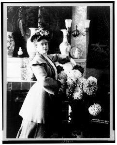 Mrs. Adna R. Chaffee, three-quarter length portrait, standing in front of fireplace, facing slightly right, with floral arrangement on the right LCCN2001699841