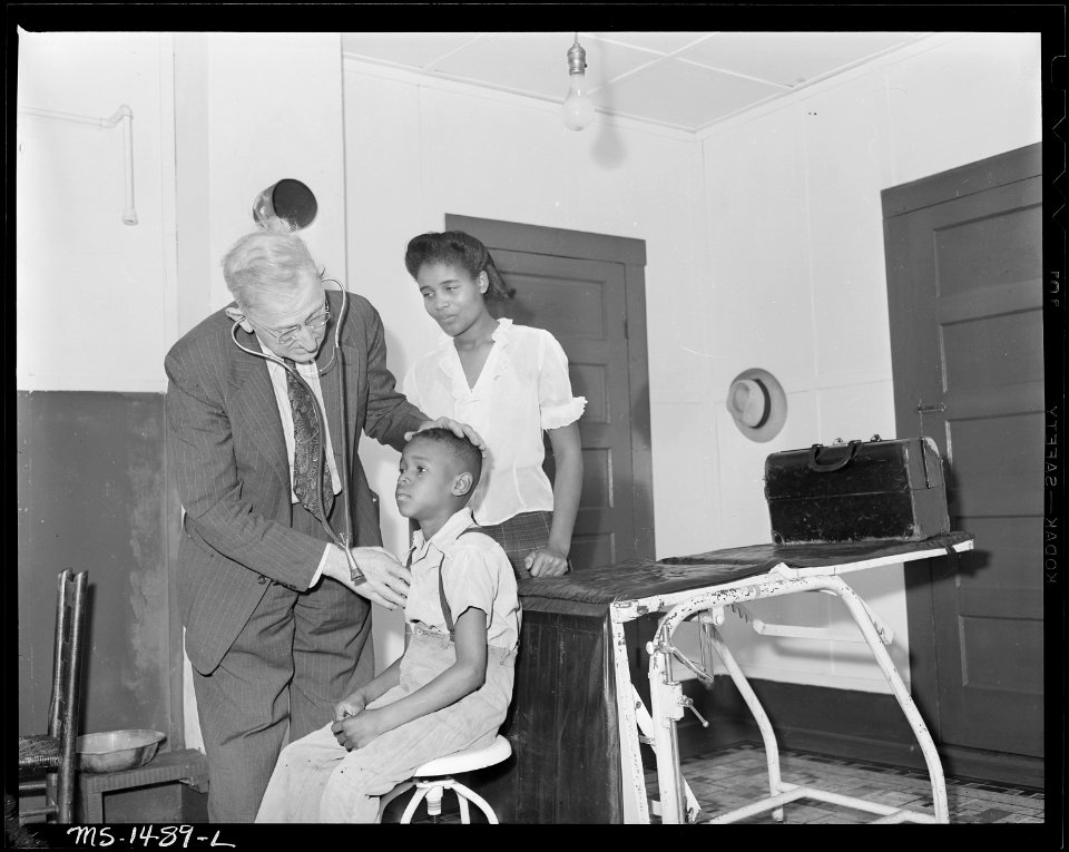 Mrs. James Robert Howard and her son with Dr. J. A. Bennet, company doctor. Dr. Bennet is in this camp office one... - NARA - 540815