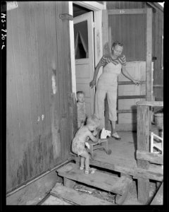 Mrs. Jack Price, wife of miner, and her two children on porch of box car home in company housing project. Note that... - NARA - 540571
