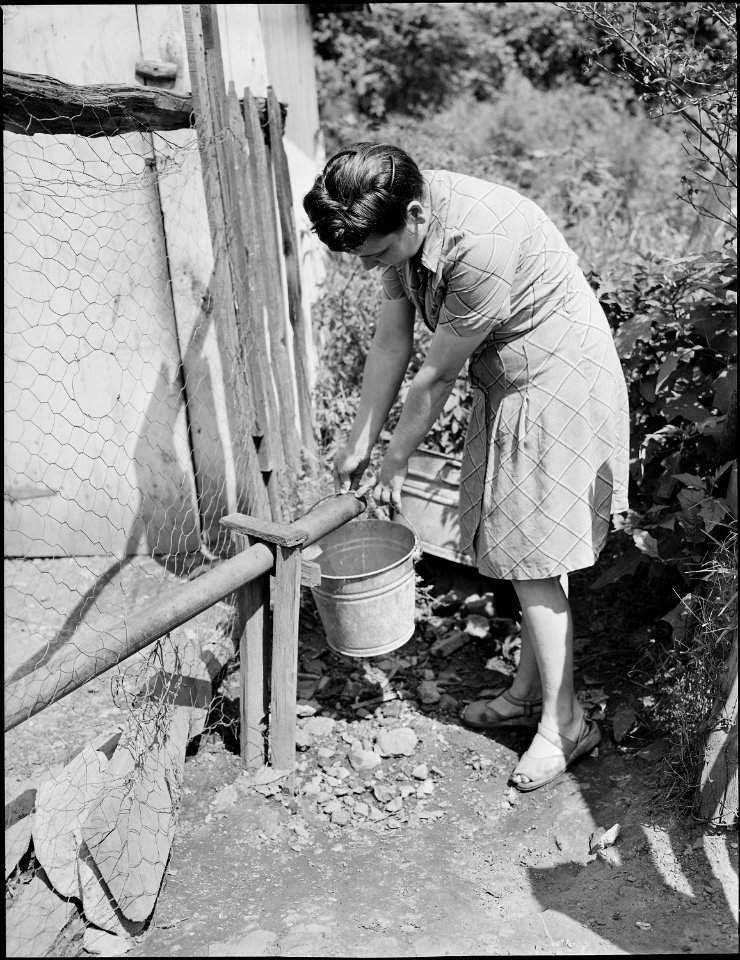 Mrs. Milong Bond getting water from slow running outside faucet. Notice the trickle of water, this is the greatest... - NARA - 540964
