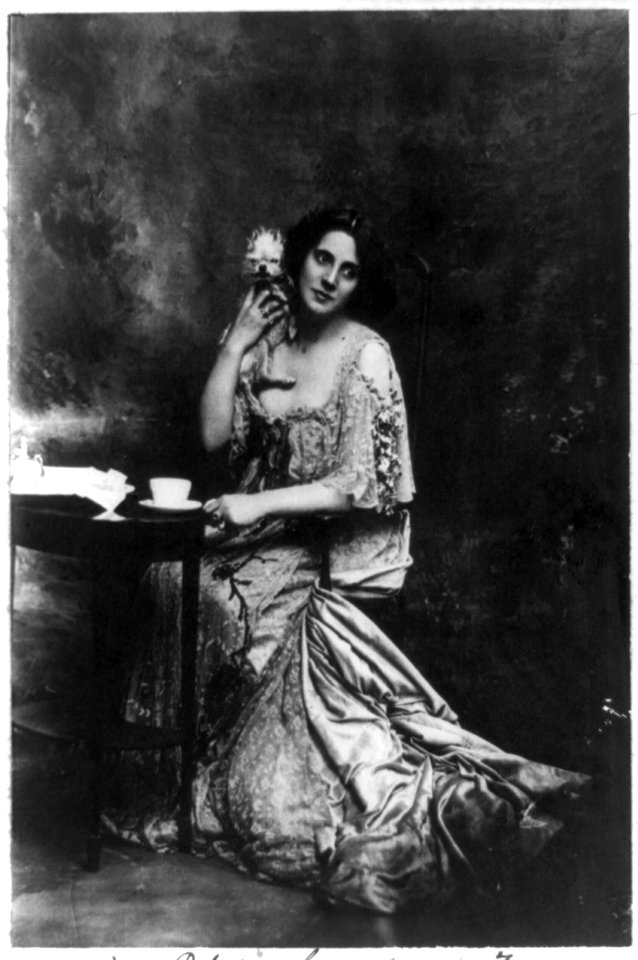 Mrs. Patrick Campbell, actress, full-length portrait, seated at small table, facing slightly right, holding pet dog LCCN90707463