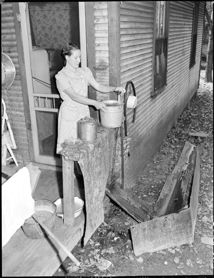 Mrs. Virgil Price, wife of miner, draws a bucket of water. Notice drainage system for this water. Black Mountain... - NARA - 541271