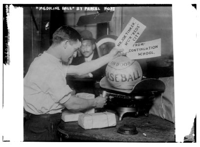 Medicine ball being weighed by Post Office employee; shipping tags read- Mr. Joe Tinker, Mgr Reds (Cincinnati) From Continuation School. (1913) LCCN2014692229