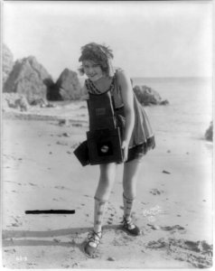 Myrtle Lind. A young woman posed with a Graflex camera on a beach LCCN2006683374