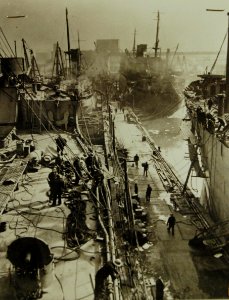 Merchant ships pull up to wharfs to have weapons installed, WWII (23554449720)