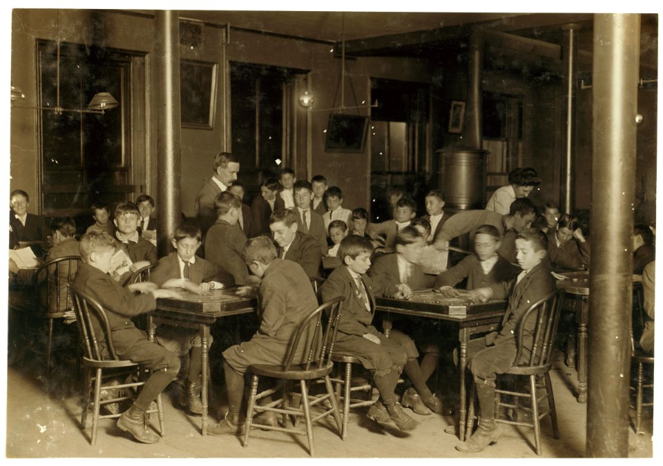 Name- In the Newsboys Reading Room. Boys seated at tables playing gamers. Boston 1915 Exhibit. Oct. 1909. LOC nclc.05433