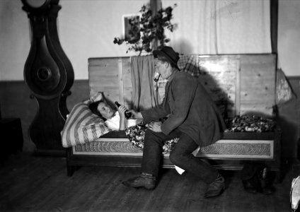 Nattfrieri. En man sitter på sängkanten och pratar med liggande kvinna och bjuder henne en flaska - Nordiska museet - NMA.0048298 photo
