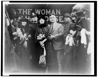 Mildred Harris Chaplin, full-length portrait, standing in crowd, facing front, guarded by a policeman LCCN96507930