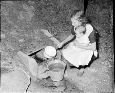 Miner's wife gets water from flowing well. She must cross the stream and carry water about a quarter of a mile to her... - NARA - 541066