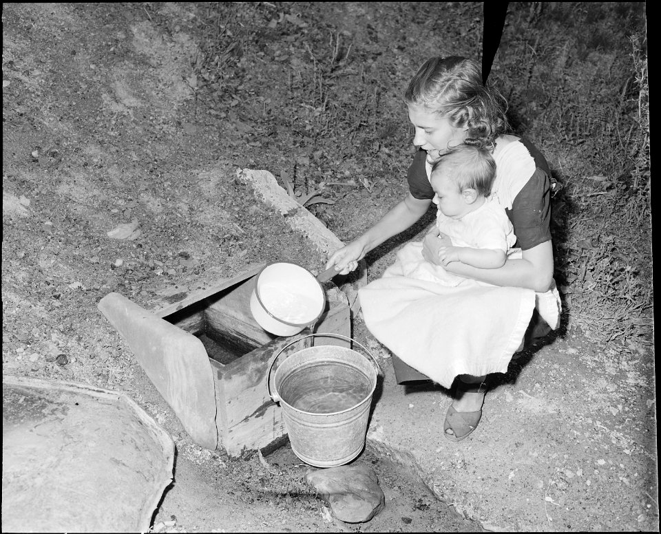 Miner's wife gets water from flowing well. She must cross the stream and carry water about a quarter of a mile to her... - NARA - 541066