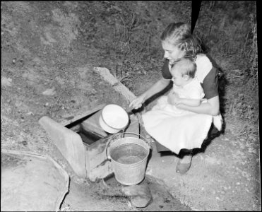 Miner's wife gets water from flowing well. She must cross the stream and carry water about a quarter of a mile to her... - NARA - 541066