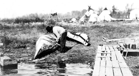 Ojibwa Indian man mending canoe by lake with teepees in 1913- LCCN90710758 (cropped) photo