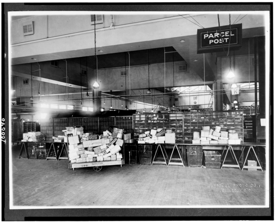 Parcel post area of mail room showing trucks and tables stacked with packages, U.S. Post Office, Washington, D.C.) - National Photo Co., Washington, D.C LCCN90709848