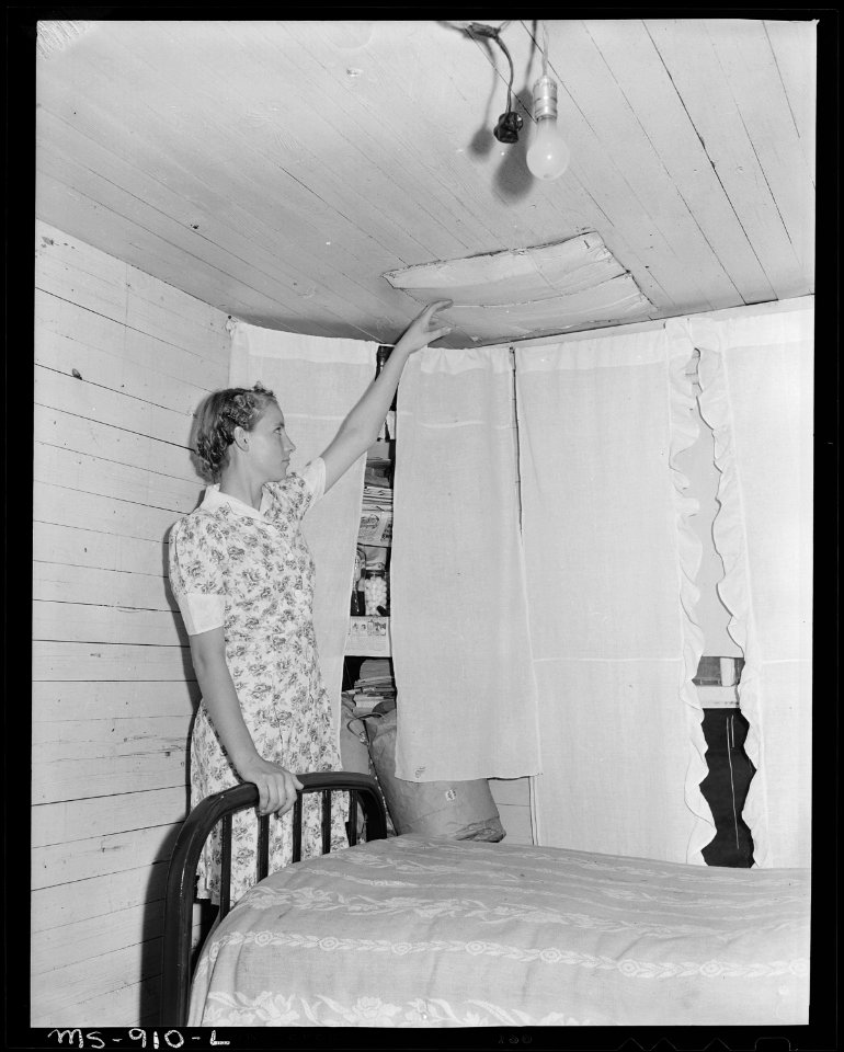 Pauline Murray, daughter of miner, pointing to metal place board which holds loose bricks of chimney from falling in... - NARA - 540606