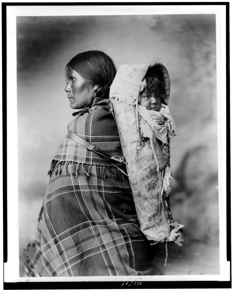 Pee-a-rat and baby - Utes. Profile of woman, half-length portrait, standing, facing left, in plaid blanket, with baby in cradleboard on her back LCCN94509882
