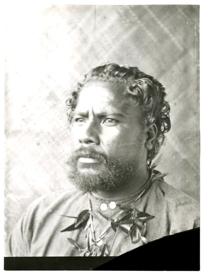 Photograph (black and white); portrait of a man with a moustache and beard, wearing a shirt and plant fibre necklace, in front of a plant fibre plaited mat on the wall; Polynesia. Gelatin silver print. Oc,B130.150, British Museum